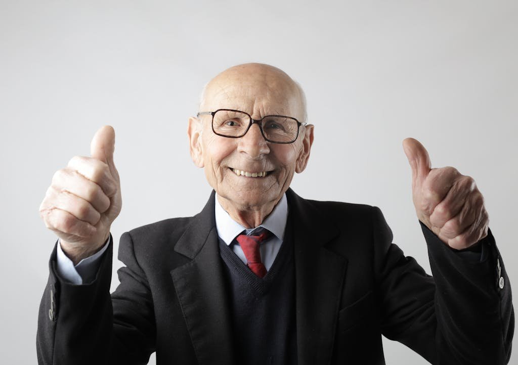 Cheerful elderly man in suit giving thumbs up, symbolizing success and approval.