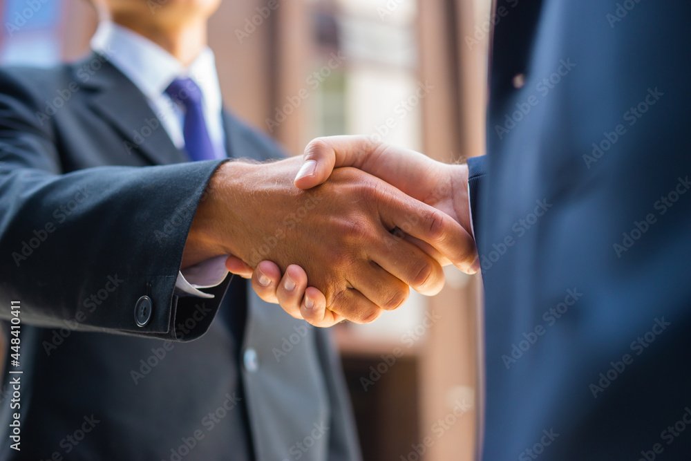Handshake close-up. Businessman and his colleague are shaking hands in front of modern office building. Financial investors outdoor. Banking and business.